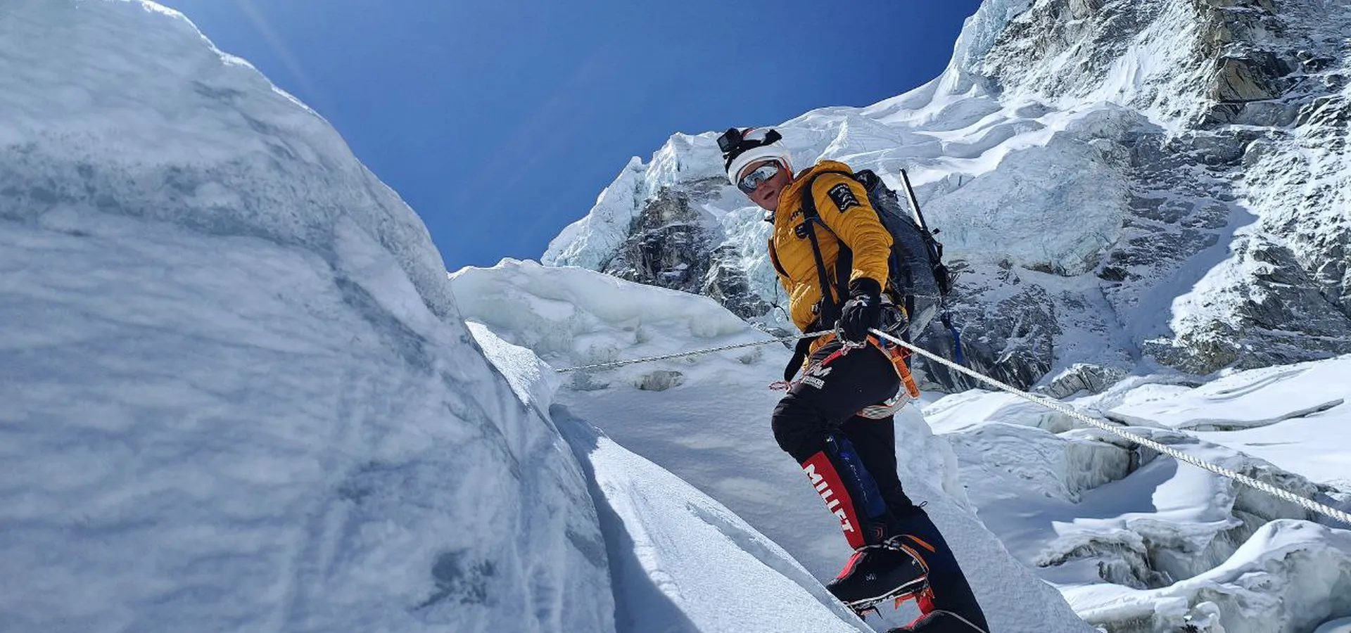 Alpiniste en doudoune jaune progressant sur une corde fixe dans une cascade de glace de l’Everest.