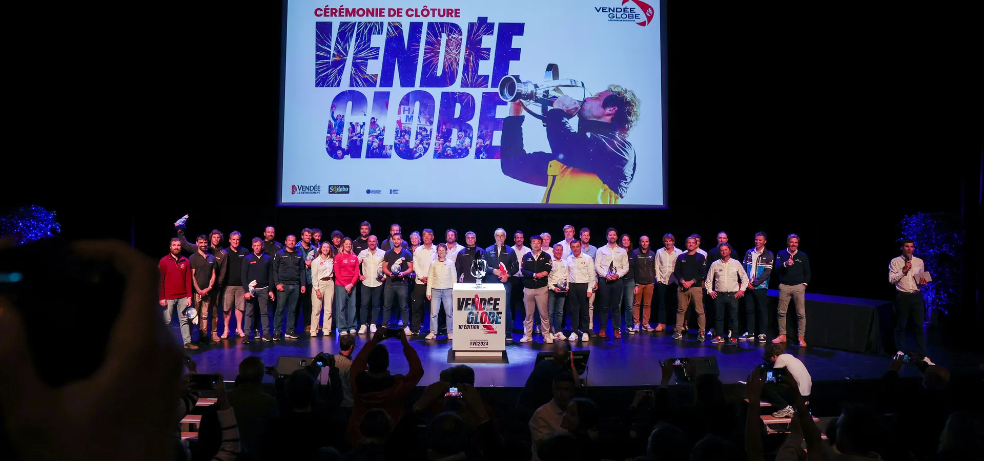 LES SABLES D'OLONNE, FRANCE - 10 MAI 2025 : Tous les skippers sont photographiés avec le vainqueur manquant MACIF Santé Prévoyance, Charlie Dalin (FRA), en arrière-plan, lors de la cérémonie de remise des prix du Vendée Globe, le 10 mai 2025 aux Sables d'Olonne, France - (Photo by Jean-Marie Liot / Alea)