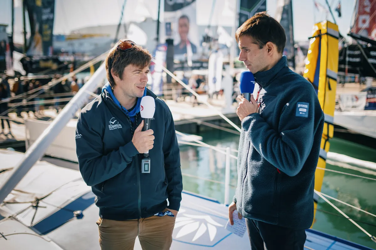 LES SABLES D'OLONNE, FRANCE - 23 OCTOBRE 2024 : Le speaker Maxime Cogny s'entretient avec le skipper de Groupe Dubreuil Sébastien Simon (FRA) pour son émission Vendée Live lors du pré-départ du Vendée Globe, le 23 octobre 2024 aux Sables d'Olonne, France - (Photo by Vincent Curutchet / Alea)