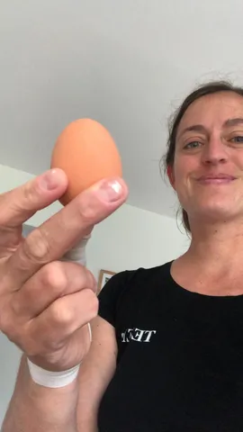 A smiling Justine Mettraux, wearing a black T-shirt, holds an egg between her index and middle fingers.